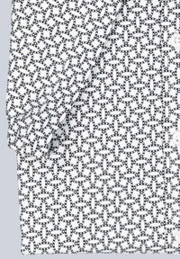 Hemd mit Kurzärmeln und weißem Hintergrund, das ein geometrisches schwarzes Muster aus miteinander verbundenen Ovale und Punktakzenten zeigt. Leichter Stoff.