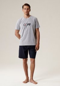 Szara bawełniana koszulka z nadrukiem "OFF" w niebieskim i czerwonym kolorze, zestawiona z ciemnoniebieskimi szortami z małym, powtarzającym się wzorem.