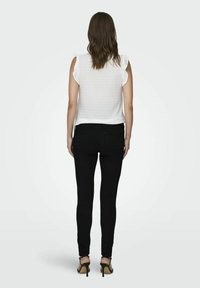 Haut sans manches blanc en tissu texturé avec des épaules volantées, associé à un jean noir ajusté et des talons hauts ouverts.