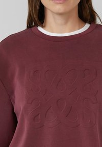 Bordeaux sweatshirt met een tekstuur, een reliëfdesign in het midden van de borst, ronde halslijn met witte rand en een gladde stoftextuur.