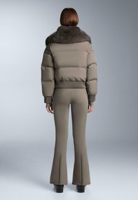 Bézs pufi dzseki szőrmés gallérral, rövidített fazonnal és bordázott mandzsettákkal. A hozzáillő, bővülő szabású nadrág szintén bézs, varrásokkal díszítve.