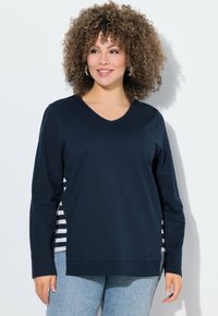 Marineblaues Langarm-V-Ausschnitt-Oberteil mit gestreiften Seitenpaneelen. Lässige Passform, weicher Stoff und gerippte Bündchen. Kombiniert mit hellblauen Jeans.