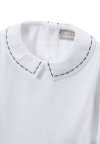 Chemisette blanche pour bébé avec col rond, ornée d'un bord noir cousu et de boutons-pression au niveau de l'encolure au dos.