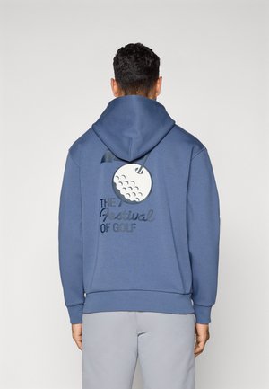 Blå bomull hettegenser med grafikk av en golfball og teksten "Festivalen for Golf" på baksiden. Inkluderer hette med snøring og ribbestrikket kant.
