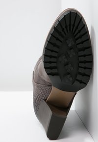 Brown leather ankle boot with textured reptile pattern, block heel, and rubber sole featuring deep grooves for traction.