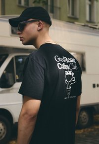 Zwarte t-shirt met de tekst "GoodRoast Coffee Club" op de achterkant, met een witte koffie kop grafiek en handontwerp.