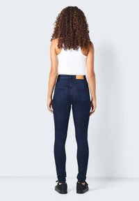 Mörkblå smala jeans i denim, med hög midja, två bakfickor och en tanläder, fyrkantig tagg vid midjan.