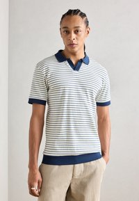 Polo rayé en blanc et marine, avec un col et des poignets côtelés. Tissu doux, à manches courtes et à coupe ajustée.