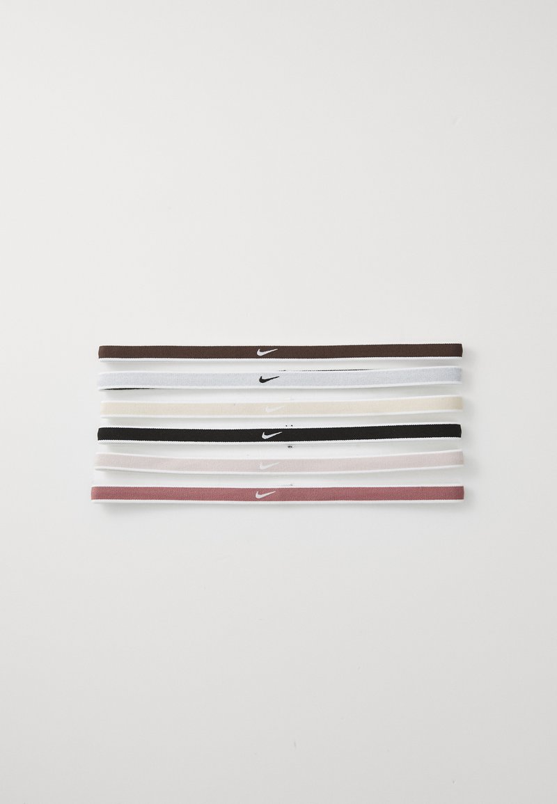 Conjunto de cinco faixas Nike nas cores castanho, branco, bege, preto e rosa. Cada faixa apresenta um pequeno logo Nike branco. Material macio e elástico.