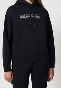 Granatowy hoodie wykonany z miękkiego materiału z nadrukiem logo z przodu. Posiada regulowany kaptur oraz ściągacze na mankietach i u dołu, co zapewnia luźny krój.