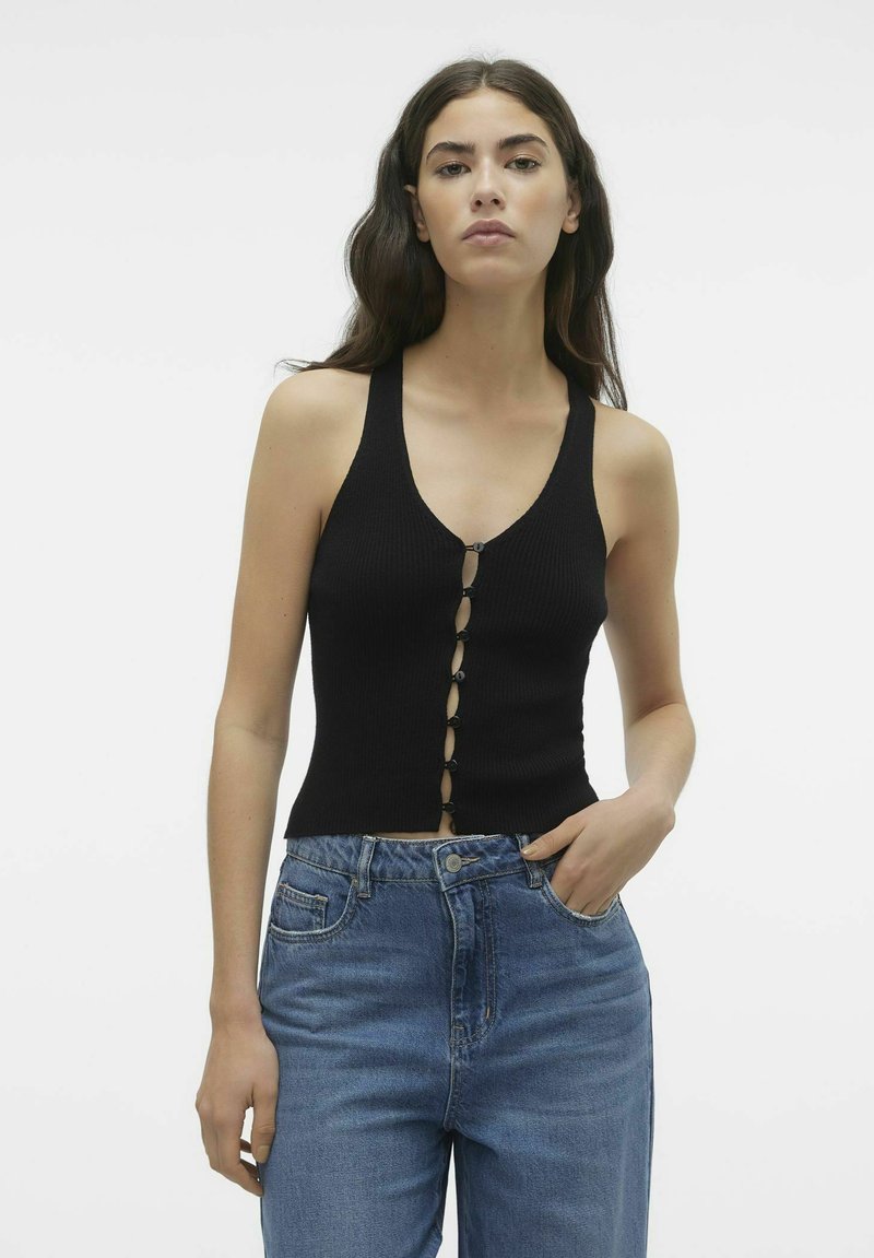 Must mustriba tank top sügava V-kaeluse ja eesnupu sulgemisega. Seljas kõrge vö�ökoha sinised teksad. Sile tekstuur, istuv disain.