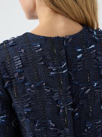 Artimiausias plano vaizdas žmogaus viršutinės nugaros, vilkinčio tamsiai mėlyną, tekstūruotą audinį su užtrauktuku ir daugiaspalviais audinio frakcionų akcentais.