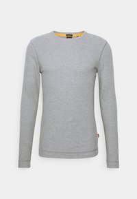 Pull à manches longues gris clair à col rond avec des détails de couture subtils et une petite étiquette orange sur la couture latérale gauche.
