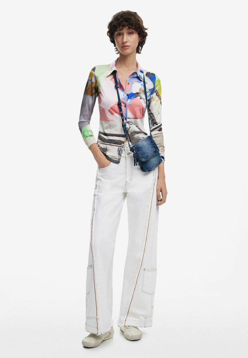 Langärmliges Hemd mit einem mehrfarbigen Blumenmuster, kombiniert mit weißen weiten Hosen und einer kleinen Jeans-Crossbody-Tasche. Helle Schuhe.