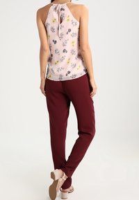 Lichtroze mouwloze top met bloemendessin, gecombineerd met bordeauxrode tapse broek en beige sandaaltjes met enkelband. Achteraanzicht.