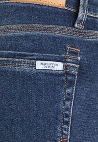 Dark blue denim jeans with gold stitching, featuring a small white label reading "Marc O'Polo DENIM" near the back pocket.
