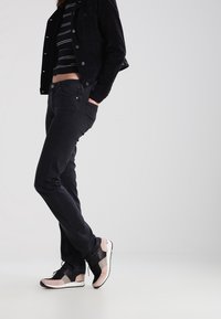 Jeans de mezclilla negra, diseño ajustado. Chaqueta negra sobre una camiseta de rayas. Las zapatillas presentan una mezcla de negro y rosa claro con suelas blancas.