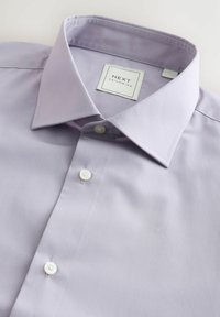 Hellblaues langärmliges Hemd mit spitzem Kragen, zwei weißen Knöpfen und einem Etikett mit der Aufschrift "NEXT TAILORING". Glatte Stoffoberfläche.