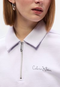 Ανοιχτό μωβ φούτερ με φερμουάρ, με γιακά και  κεντημένο λογότυπο "Calvin Klein" στο στήθος, με λεία υφή και μεταλλικό φερμουάρ.