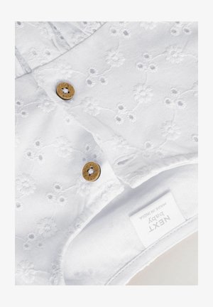 Biały bawełniany kombinezon dla niemowląt z haftem kwiatowym, z dwoma złotymi guzikami i metką. Miękka tekstura i dopasowany krój zapewniający komfort.