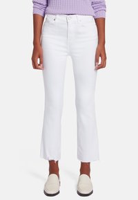 Jean flare blancs à taille haute, avec un ourlet effiloché et un design classique à 5 poches. Porté avec un pull en tricot violet clair et des mocassins.