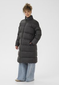 Cappotto puffo nero con colletto alto, caratterizzato da un design trapuntato e chiusura con zip. Abbinato a pantaloni in denim chiaro a gamba larga.