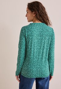 Langärmliges Hemd aus einem türkisgrünen Stoff mit einem subtilen abstrakten Muster. Weiche Textur, runder Ausschnitt und lässige Passform mit abgerundetem Saum.
