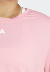 Camiseta deportiva de color rosa claro, hecha de una tela suave, con un escote redondo y un pequeño logo blanco en la parte superior izquierda.