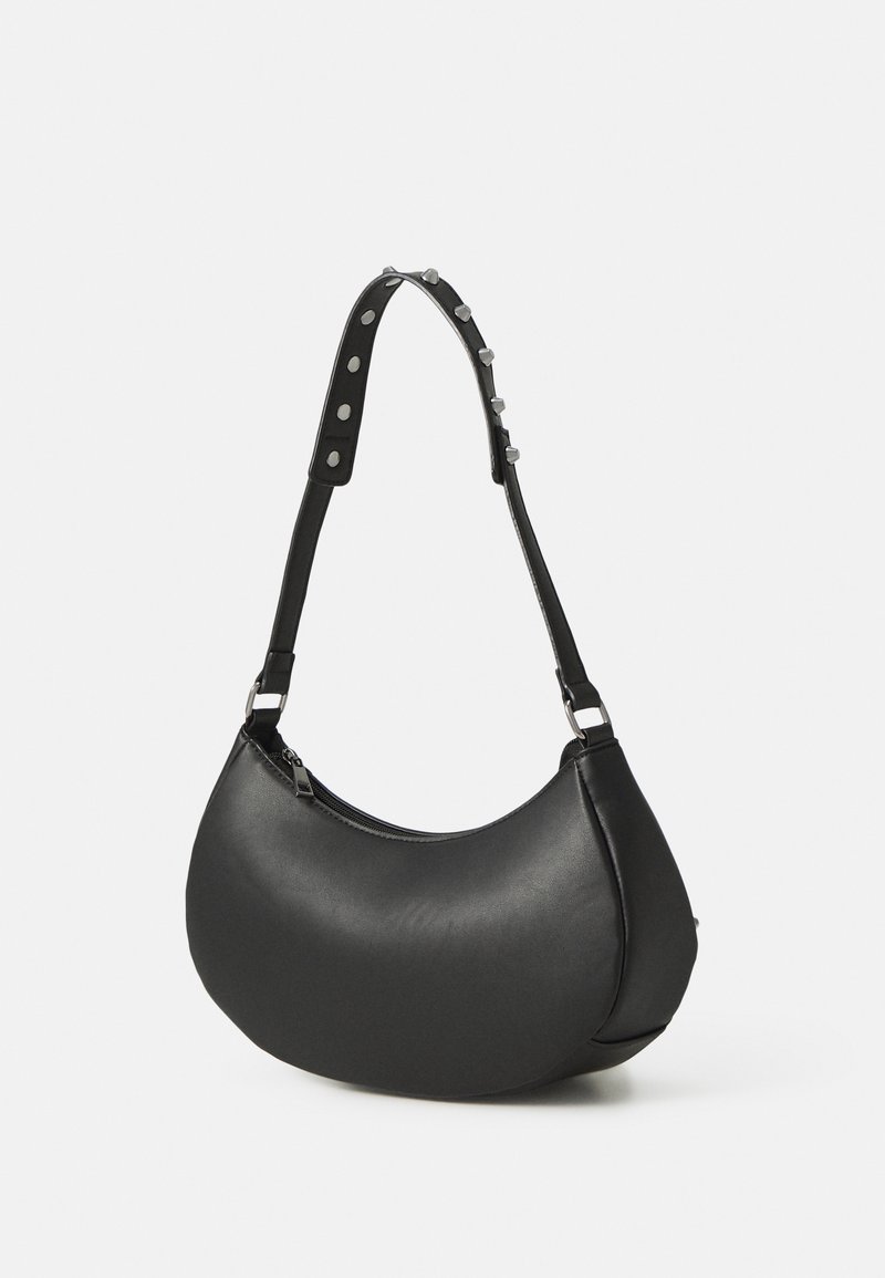 Sac à main noir en forme de croissant avec fermeture éclair et bandoulière réglable, orné de clous argentés et d’accents métalliques circulaires.