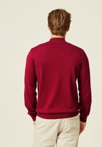 Maglione bordeaux in maglia con maniche lunghe e colletto a coste, caratterizzato da un orlo aderente. Tessuto morbido, design semplice, senza motivi o decorazioni visibili.