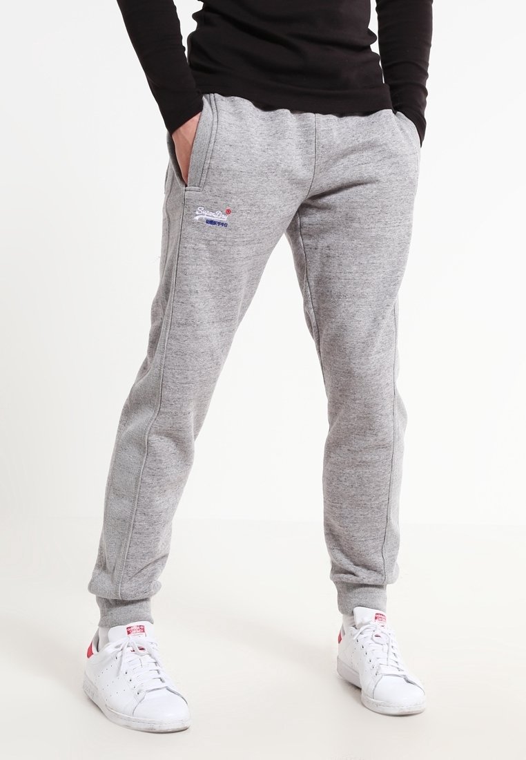 Graue Jogginghosen aus Baumwolle mit schlanker Passform, ausgestattet mit einem elastischen Bund, Seitentaschen und einem kleinen Logo am Bein. Kombiniert mit weißen Turnschuhen.