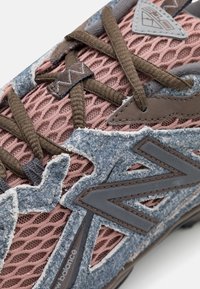 Sneakers a rete viola e blu con dettagli testurizzati, lacci marroni e un grande logo "N" grigio sui lati.