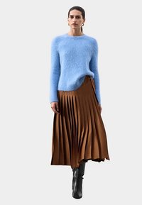 Světle modrý nadýchaný svetr v kombinaci s hnědou plisovanou sukní. Černé kozačky nad kolena doplňují outfit. Jednoduchý, moderní střih a textury.