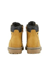 Schwarze Stiefeletten aus Wildleder mit schwarzen Kunstfellbesätzen, seitlichen Reißverschlüssen und robusten braunen Laufsohlen, die für Halt sorgen.