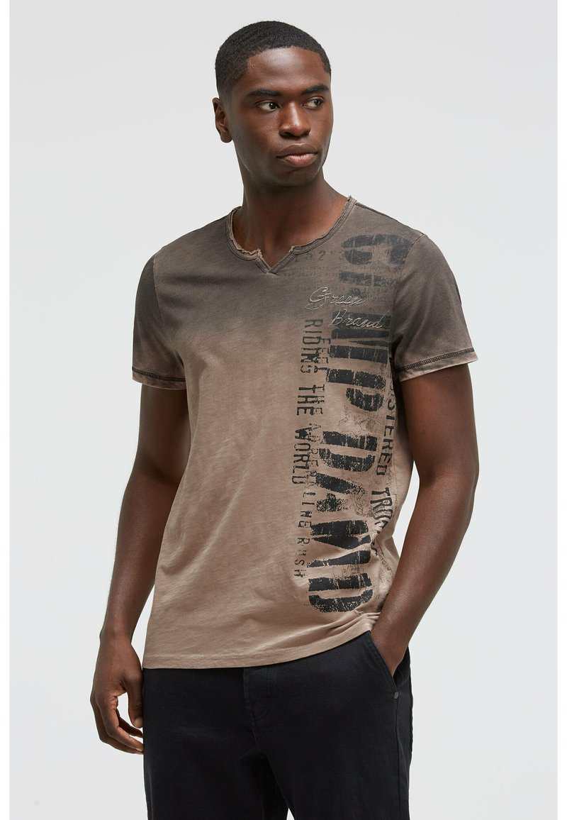 Short-sleeve, v-neck t-shirt in gradient brown tones. Features black text graphics along one side and a slightly distressed finish.