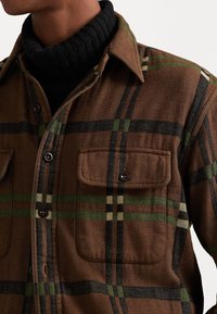 Barna kockás ing, amely szövetből készült; zöld és fekete vonalakkal, gombos elülső résszel, két mellzsebbel és klasszikus gallérral rendelkezik.