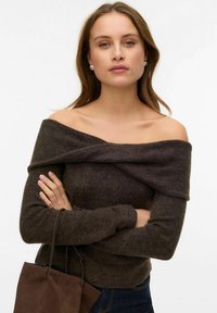 Pull marron à épaules dénudées avec texture côtelée, manches longues et encolure drapée. Associé à un sac en daim marron.