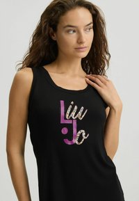 Mustamatahene musta särk, millel on läikiv mitmevärviline "Liu Jo" logo lilas ja mustritega aktsendid. Pehme kangas ja lõdva lõikega.
