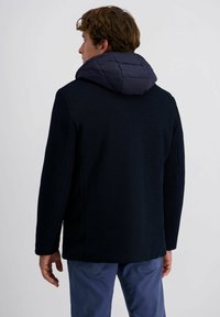 Marineblaue gerippte Jacke mit abnehmbarer Daunenkapuze. Merkmale sind lange Ärmel, ein gerader Schnitt und eine strukturierte Oberfläche. Rückansicht dargestellt.