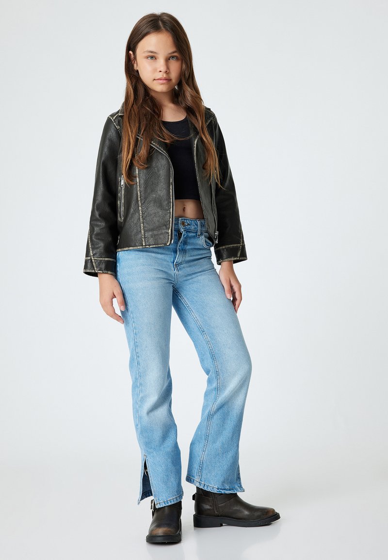 Chaqueta corta de cuero negro con costuras en contraste, combinada con jeans acampanados de color azul claro con cremalleras laterales y botas negras hasta el tobillo.
