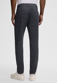Dunkelgraue, texturierte Hose mit schlanker Passform und zwei Gesäßtaschen. Kombiniert mit hellen Sneakers, die einen zeitgemäßen, lässigen Stil zeigen.