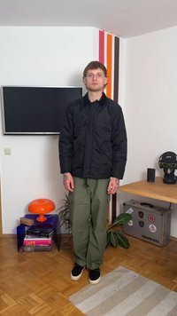 Juodas paminkštintas švarkas su aukštu apykakle, užsegamas įmautėmis, ir priekinėmis kišenėmis, derinamas su alyvuogių žaliais laisvo kirpimo kelnėmis ir juodais batais.