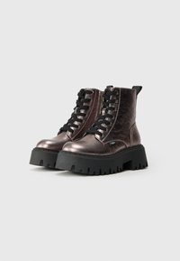 Par de botas de tobillo metálicas moradas con cordones y suelas de plataforma negras gruesas, con cremalleras laterales, sobre un fondo claro y sencillo.