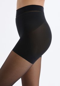 Collant neri trasparenti con una solida fascia alta in vita, texture liscia e una transizione a nero opaco sui cosci.