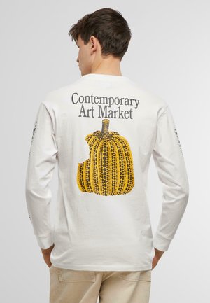 Long-sleeve white T-shirt featuring a yellow pumpkin graphic with black dotted patterns and text reading "Contemporary Art Market" on the back.