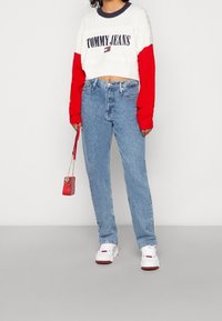 Pull court rouge et blanc avec le logo "TOMMY JEANS", associé à un jean taille haute bleu clair et des baskets blanches. Petit sac à main rouge.
