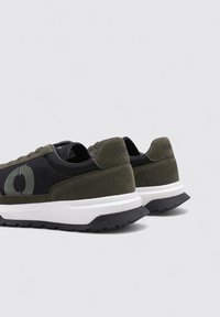 Zapatillas verdes y negras con parte superior de ante y malla, que presentan un logotipo circular, entresuela blanca y suela negra texturizada.