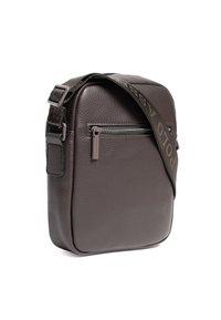 Hnědá kožená crossbody taška s texturovaným povrchem, která má přední kapsu na zip a vzorovaný nastavitelný popruh.