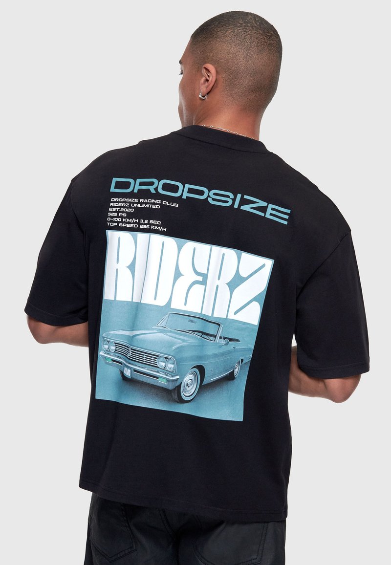 Homme portant un t-shirt noir avec une voiture décapotable vintage bleue et un grand texte "RIDERZ" imprimé dans le dos.