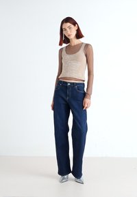 Světlý béžový crop top na tělo vrstvený přes průsvitnou košili s dlouhým rukávem, spárovaný s tmavě modrými širokými džínami a stříbrnými lodičkami se špičatou špičkou.